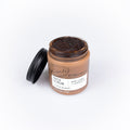 Jar of face scrub with a black lid on a white background