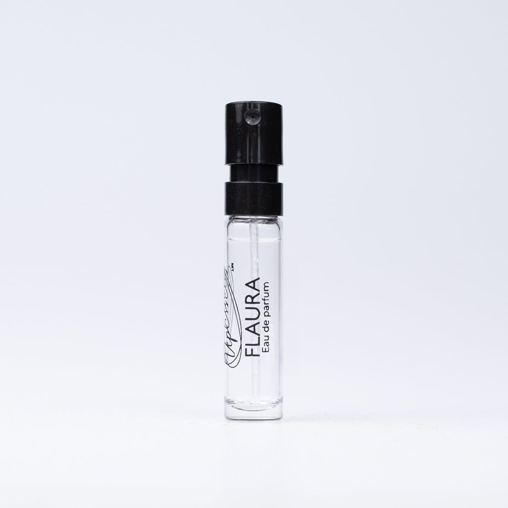 A clear glass perfume sample spray bottle with a black atomizer cap, labeled 'FLAURA Eau de parfum', set against a plain white background.