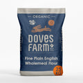 A 25 kg bag of Doves Farm Organic Fine Plain English Wholemeal Flour. The packaging is dark blue with white text and illustrations of a rabbit, bee, and sun, with an orange circular badge indicating '25 KG'.