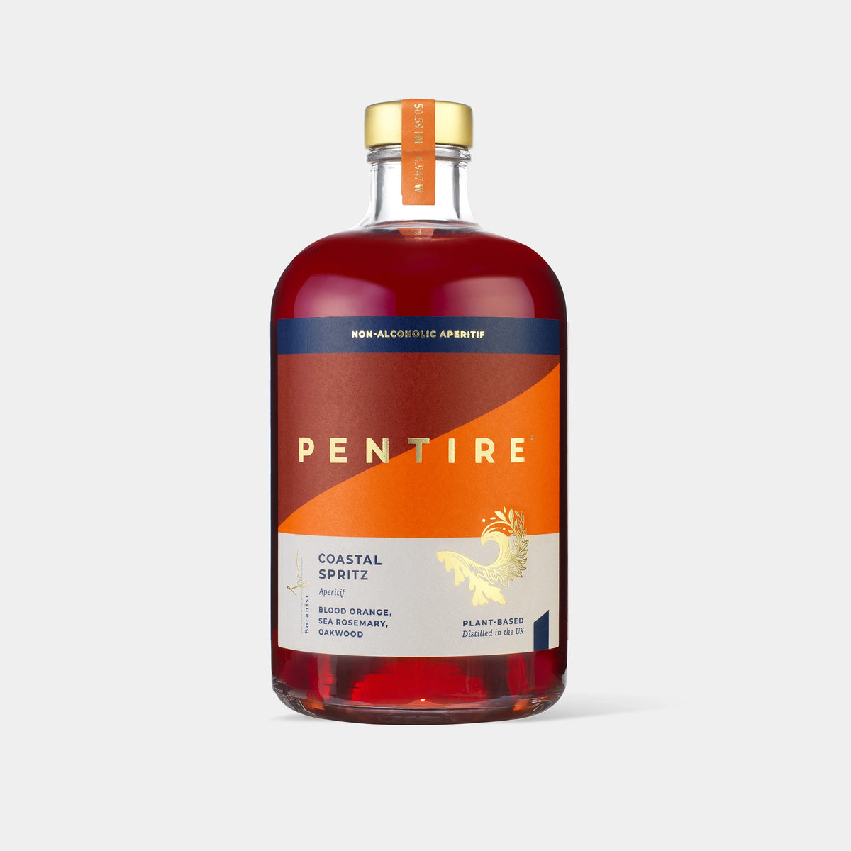 A bottle of Pentire Coastal Spritz non-alcoholic aperitif on a light gray background. The bottle is made of clear glass showing a reddish-brown liquid inside, with a gold cap and a label featuring orange, navy blue, and white sections.