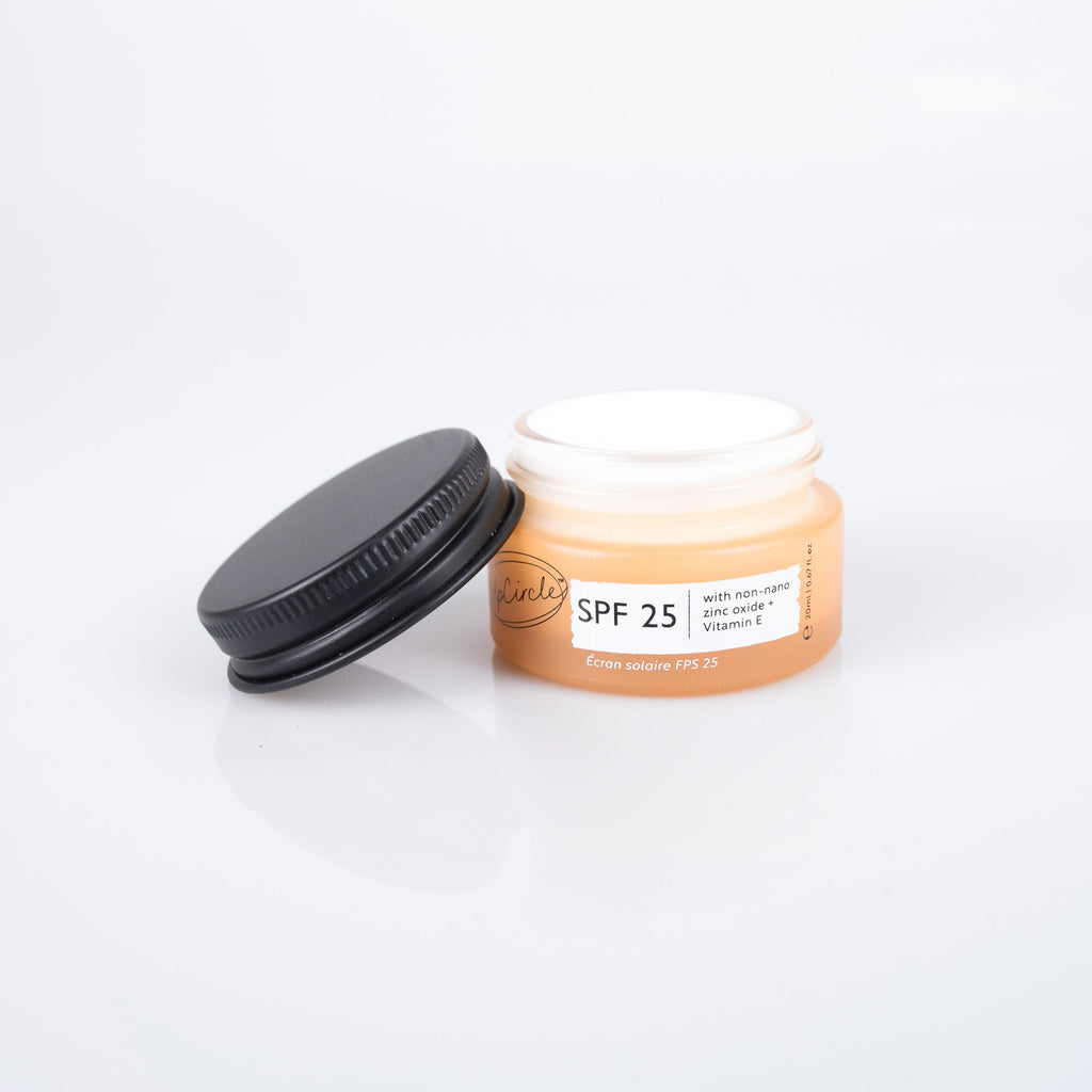 An open jar of SPF 25 sunscreen cream with a black lid resting beside it on a clean white background.
