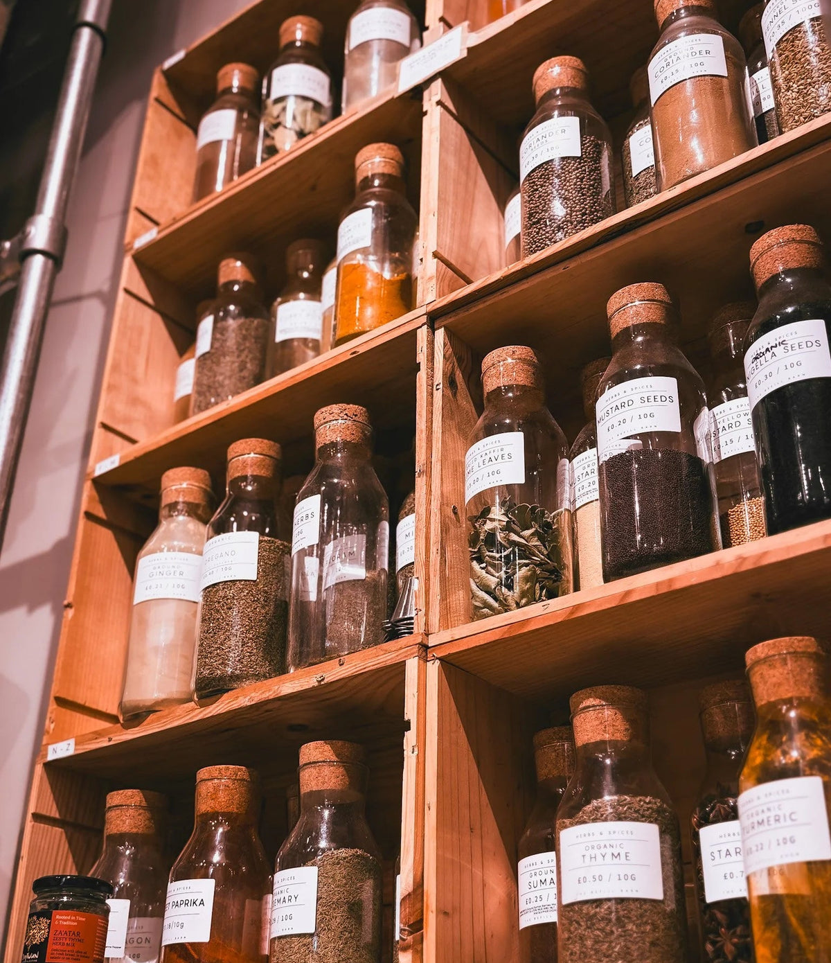 A wooden shelving unit filled with glass apothecary-style bottles containing dried herbs, spices, and liquids, each with white handwritten labels.