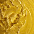 A close-up texture shot of a thick, creamy yellow-orange paste with a glossy, whipped consistency.