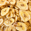 A close-up pile of dried banana chips with golden-yellow to light brown tones and darker brown centers.