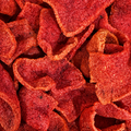 A close-up pile of red-orange, crispy, curled snack chips heavily coated with a fine red seasoning, filling the entire frame.