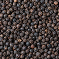 A close-up, top-down view of a dense pile of whole black peppercorns filling the entire frame.