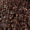A close-up of a dark brown to black coarse ground spice or herb pile, with some reddish-brown flecks visible, filling the entire frame. 
