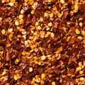 A close-up, top-down view of dried red chili pepper flakes mixed with yellow-orange seed pieces, filling the entire frame.