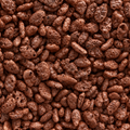 A close-up, top-down view of brown porous puffy snack pieces, resembling rice krispies or chocolate-coated popcorn kernels, filling the entire frame.