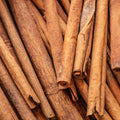 A close-up pile of whole cinnamon sticks with natural brown and tan tones, filling the entire frame.