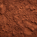 A close-up texture shot of a fine, granular reddish-brown cocoa powder, filling the entire frame. 