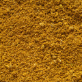 A close-up texture shot of a fine, granular golden-brown curry powder, filling the entire frame.