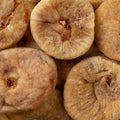 A close-up pile of dried figs, showing their wrinkled, tan-brown textured surfaces.
