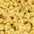 A close-up of organic white farfalle bow shaped dried pasta filling the entire frame. 