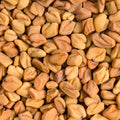 A close-up, top-down view of fenugreek seeds filling the entire frame, showing their natural tan and light brown colors.