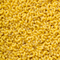 A close-up, top-down view of numerous small elbow macaroni pasta pieces filling the entire frame, showing their characteristic curved shape and hollow centers.