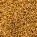 A close-up texture shot of a fine, granular golden-brown cumin powder, filling the entire frame. 