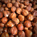 A close-up view features a plentiful pile of hazelnuts. The nuts fill the entire frame, creating a textured, organic pattern.