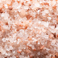 An extreme close up shows many pieces of translucent, angular, and light pink Himalayan salt.