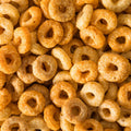 This close-up photograph showcases a heap of ring-shaped toasted grain cereals, their colors ranging from light yellow to dark orange.