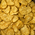 A close-up, top-down view of golden-brown potato chips piled together, filling the entire frame.
