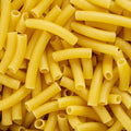 A close-up, top-down view of yellow macaroni pasta pieces piled together, filling the entire frame.