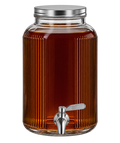 A large ribbed clear glass beverage dispenser filled with amber liquid, featuring a silver metal lid and a chrome spout with a white handle, isolated on a white background.