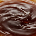 A close-up of glossy, dark brown caramel or chocolate sauce with smooth ripples and a glossy finish.