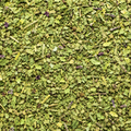 A close-up, top-down view of dried herbal spice blemd, featuring green leaves, stems, and small purple flower petals mixed together.