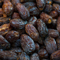A close-up pile of dark brown medjool dates with glossy, wrinkled skins filling the frame.