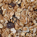 A close-up, top-down view of a granola mixture containing rolled oats, toasted flakes, and dark dried fruit pieces.