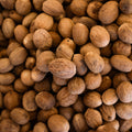 A close-up pile of brown, oval-shaped whole nutmeg seeds with textured, rough outer shells.