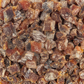 A close-up view of chopped dried fruit pieces, likely apricot or peach dried slices, showing a mix of deep brown, amber, and dark brown tones with a dusty sugar coating.