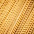 A close-up texture shot of uncooked spaghetti noodles, showing the diagonal alignment of thin, light tan pasta strands.