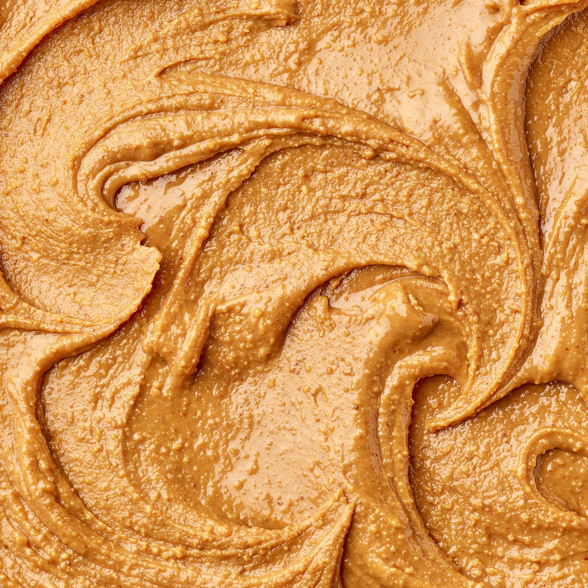 A close-up texture shot of a thick, creamy peanut butter with smooth, swirled swirls.