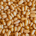 This close-up shot showcases a large group of raw pine nuts, with their smooth textures and pale yellow color filling the frame.
