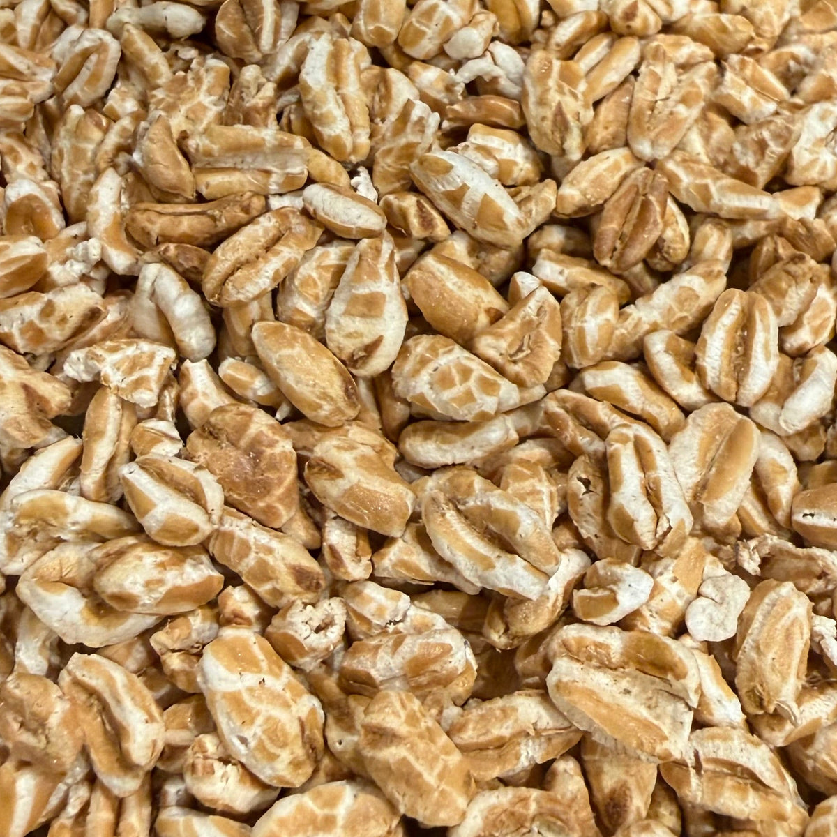 A close-up, top-down view of golden-brown popcorn kernels piled together, filling the entire frame.