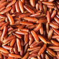 An extreme close-up shot shows numerous grains of raw red rice filling the frame, creating a textured and visually rich composition. 