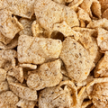 A close-up view of a pile of textured, light tan shiitake mushroom crisps, filling the frame.