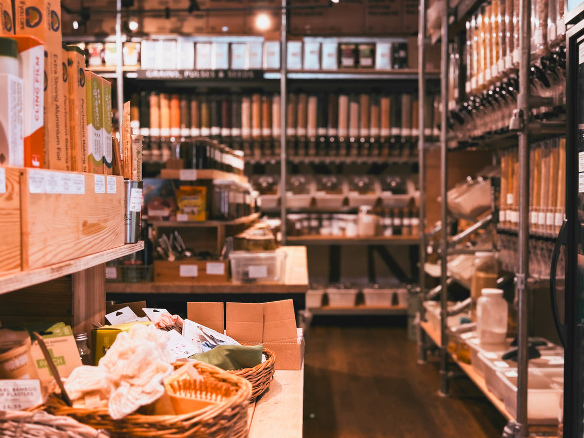 Interior of a store with shelves stocked with products and a basket of bread on a table.