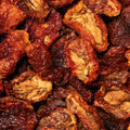 A close-up pile of dried sun-dried tomato halves showing their wrinkled, dark reddish-brown outer skins and lighter tan inner areas.
