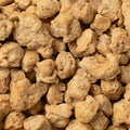 A close-up shot shows a pile of dried, light brown textured vegetable protein. The pieces are irregular in shape and have a slightly rough texture. 