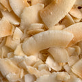 A close-up perspective reveals a pile of toasted coconut chips. The chips display a mix of white and yellow hues with slightly browned edges. 