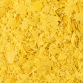 Close-up of bright yellow nutritional yeast flakes, filling the entire frame. 