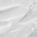 A close-up texture shot of a thick, creamy white cosmetic cream with smooth, glossy swirled strokes.