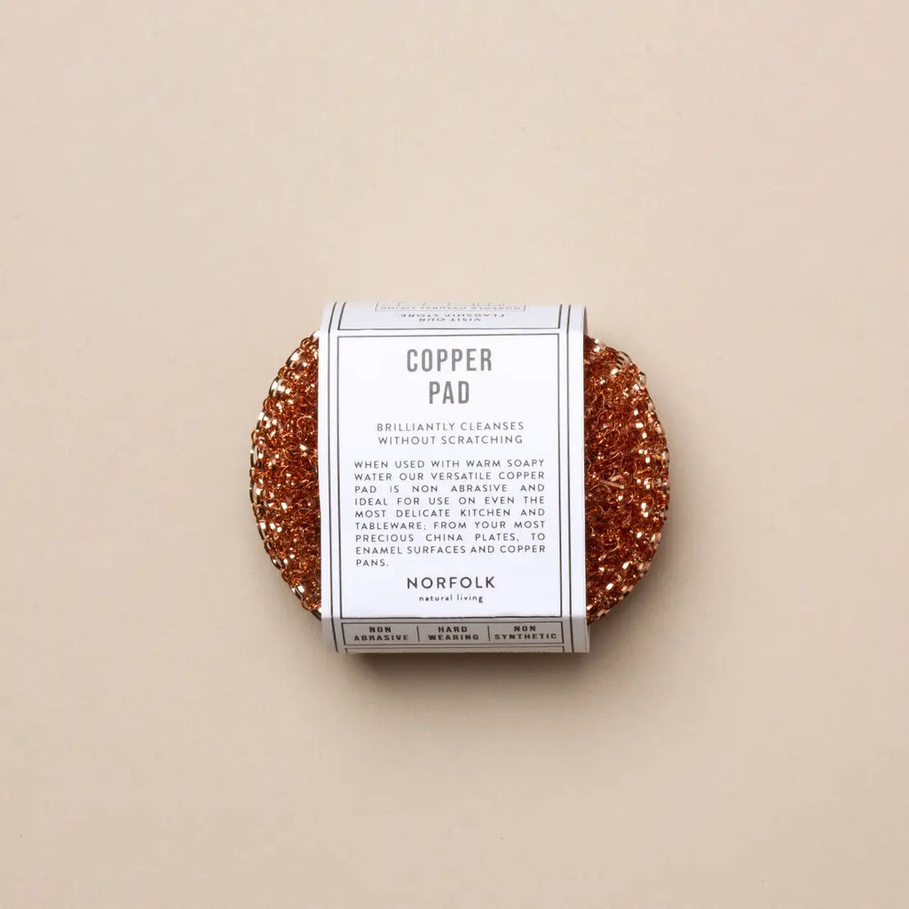 A copper pad cleaning sponge wrapped in a white paper band labeled 'COPPER PAD' and 'NORFOLK', centered on a warm beige background.
